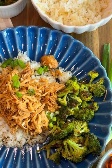 crockpot mongolian chicken with rice, broccoli on blue plate. green onions, carrots, rice in bowl and broccoli in bowl around plate