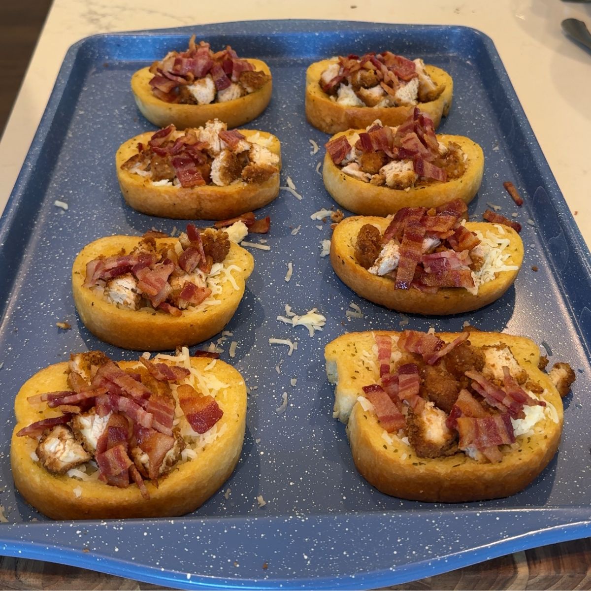 bacon, chicken and cheese on top of texas toast on blue sheet pan