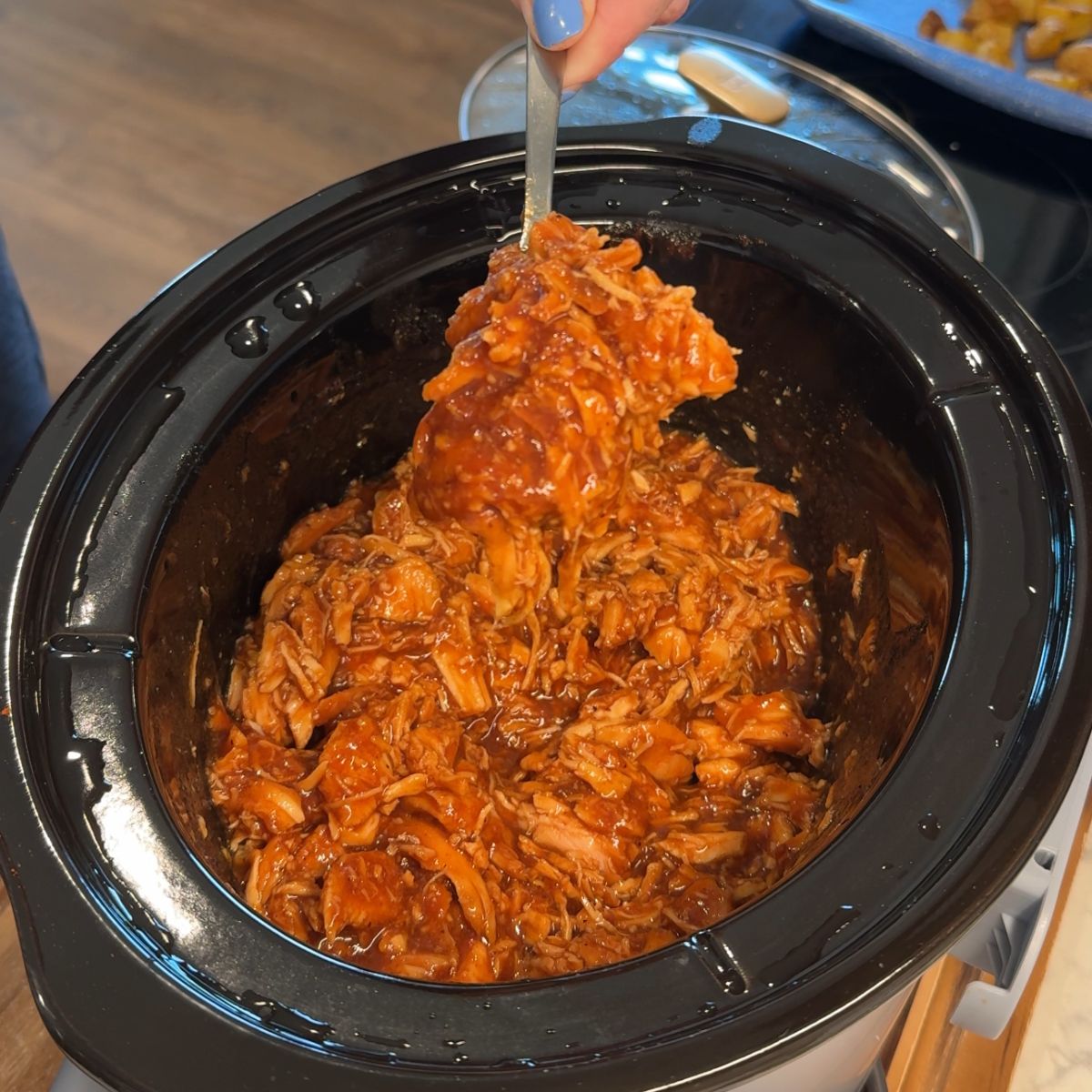 bbq chicken in slow cooker with spoon holding chicken over the pot