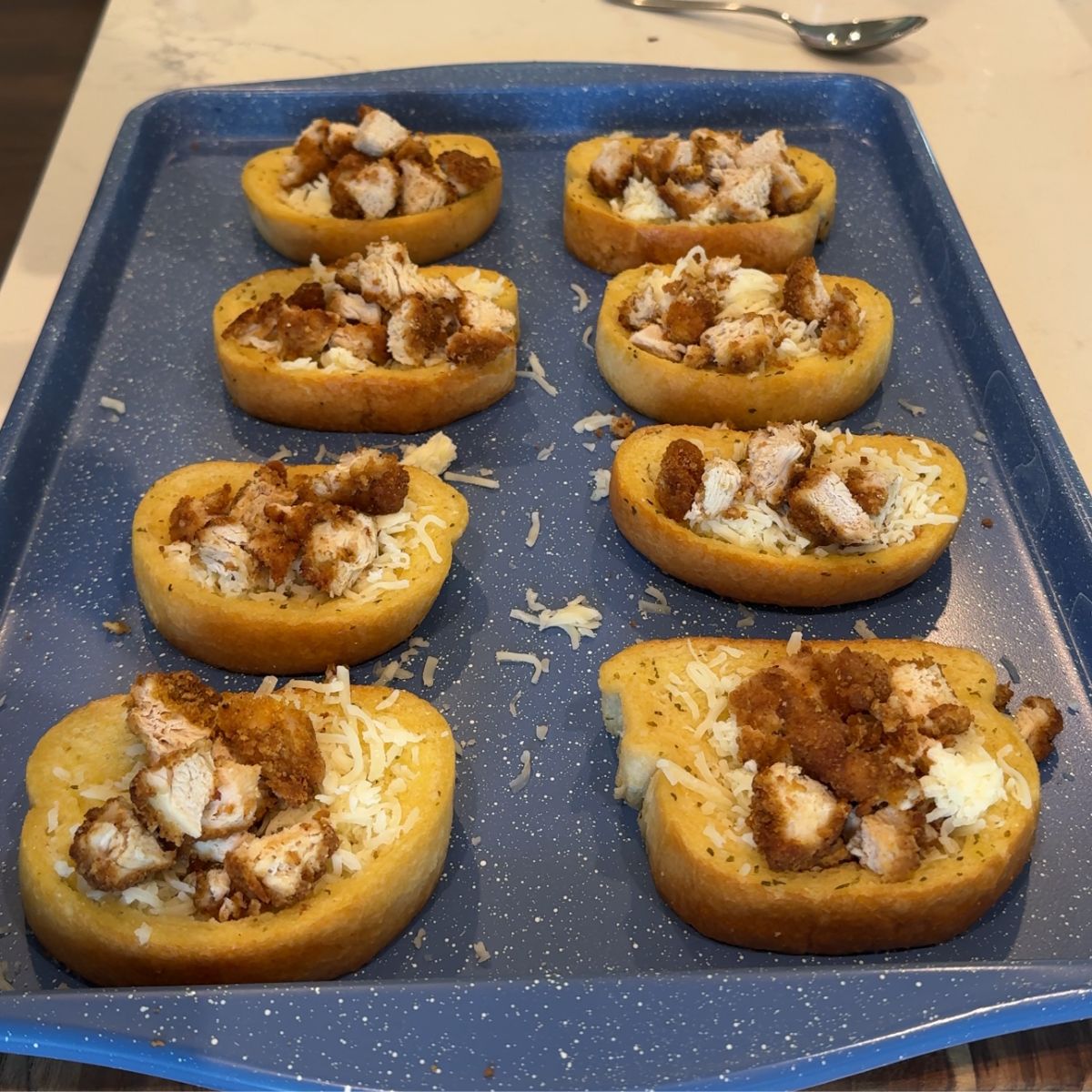 chopped and cooked chicken on top of cheese and texas toast on blue sheet pan