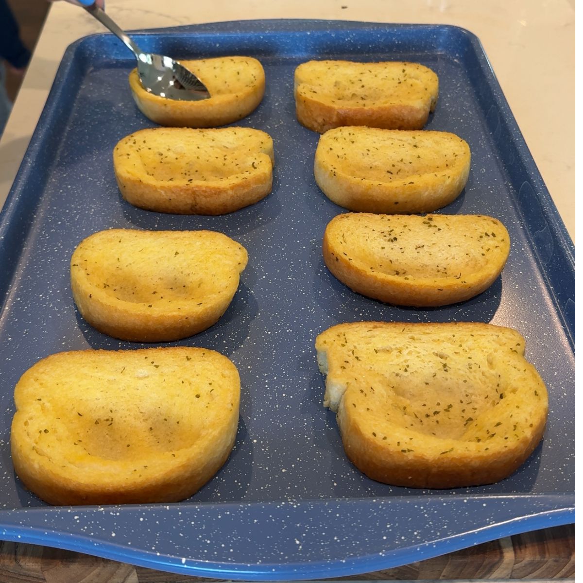 spoon over texas toast pressing down to create boat for ingredients on blue sheet pan