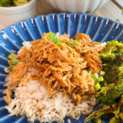 crockpot mongolian chicken on blue plate. rice in bowl in background and broccoli in white cup