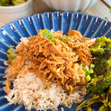 crockpot mongolian chicken on blue plate. rice in bowl in background and broccoli in white cup