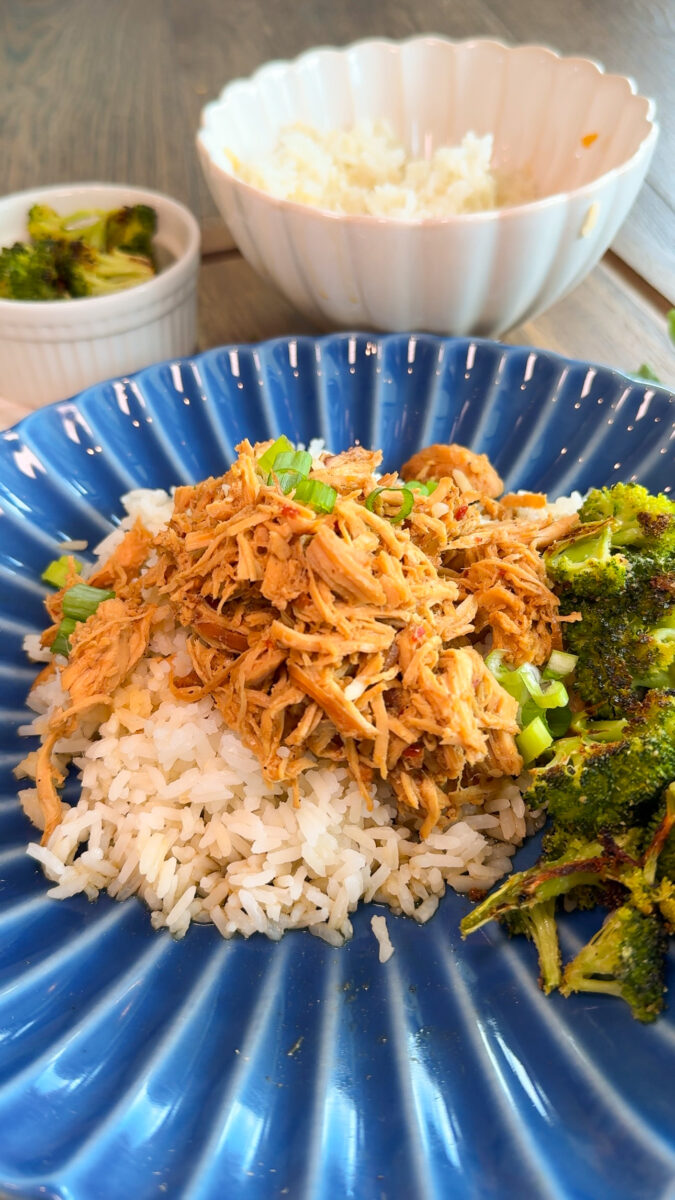 crockpot mongolian chicken on blue plate. rice in bowl in background and broccoli in white cup