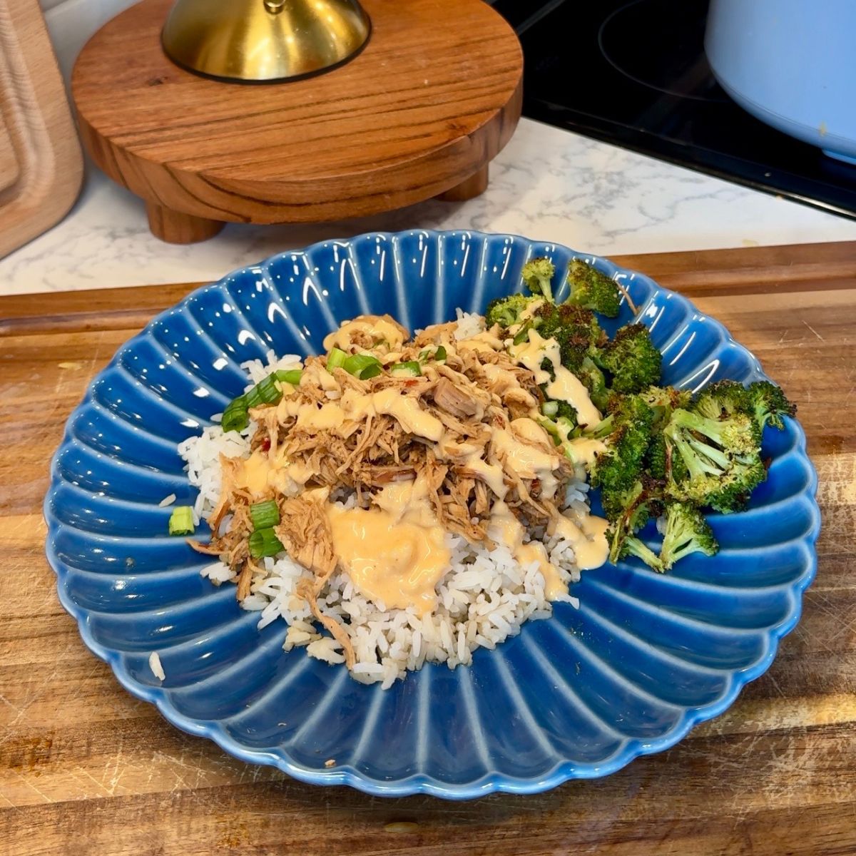 slow cooker mongolian chicken on blue plate with rice and broccoli. sauce drizzled on top with green onions