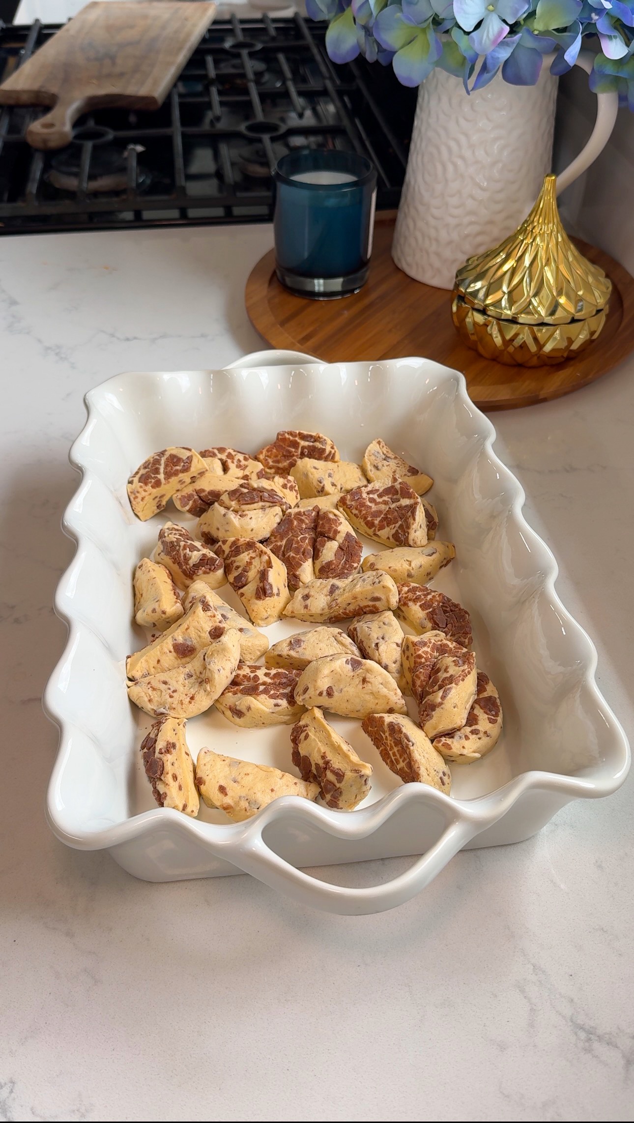 A white baking dish filled with sliced cookie dough sits on a kitchen counter near a stove, with decorative items and a candle in the background.