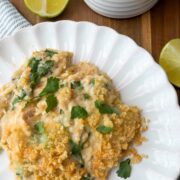 A serving of creamy casserole topped with breadcrumbs and fresh herbs on a white plate, with lime wedges and a bowl of uncooked orzo pasta nearby on a wooden surface.