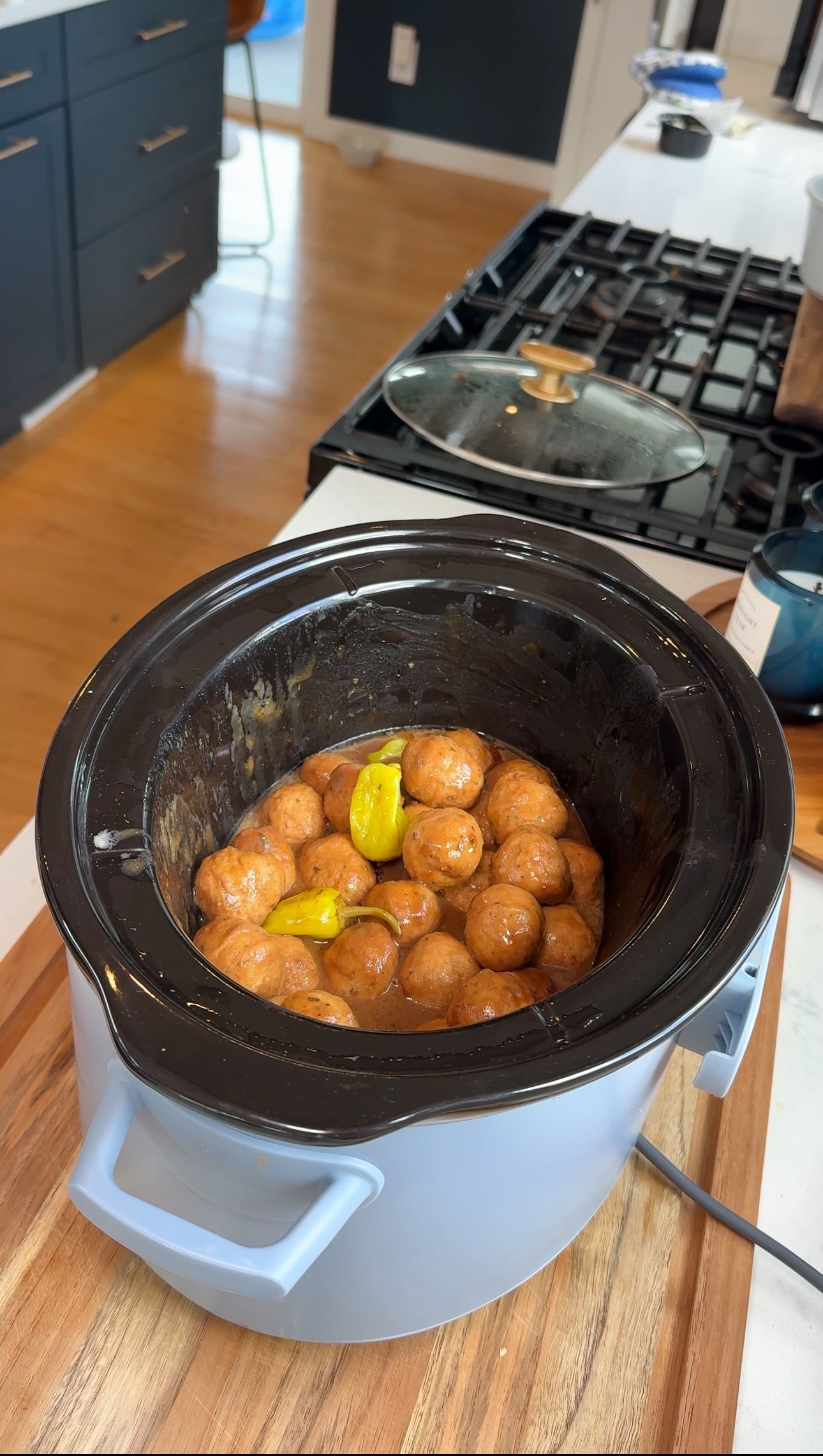 A slow cooker on a kitchen counter contains small round potatoes and a few pieces of butter or margarine on top, ready to be cooked.