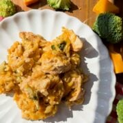 A plate of chicken broccoli orzo casserole with melted cheddar, surrounded by broccoli florets, cheddar cheese, and an onion.
