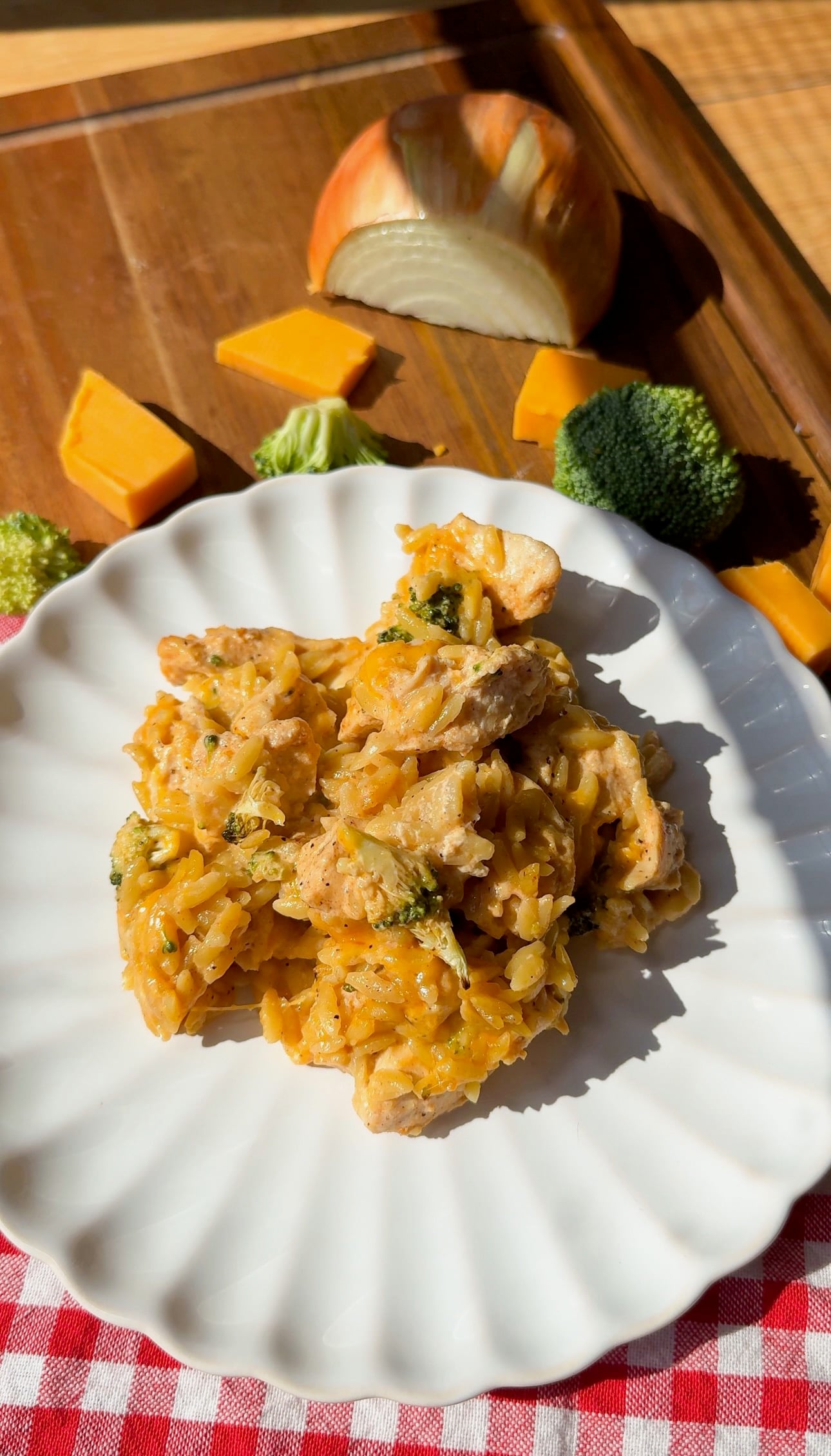 A serving of broccoli cheddar orzo with chicken on a white scalloped plate.
