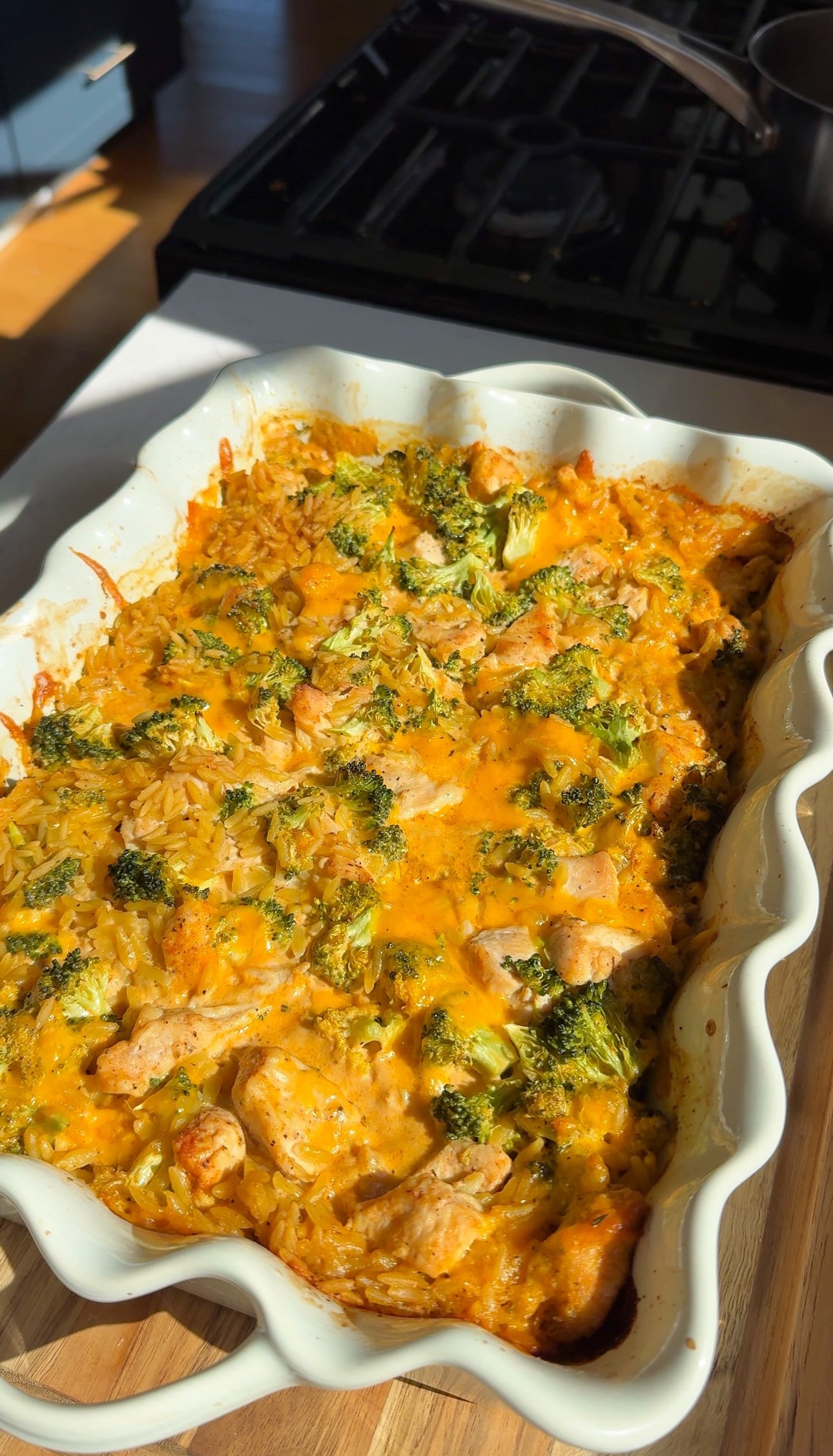 Baked chicken broccoli orzo casserole with bubbly melted cheddar in a white scalloped baking dish.