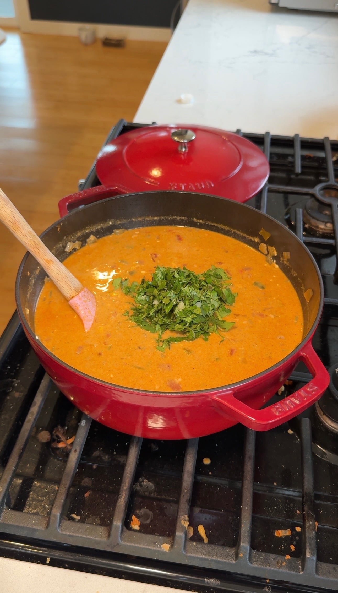 Creamy chicken tortilla soup with chopped cilantro being stirred with a wooden spoon in a red Dutch oven.