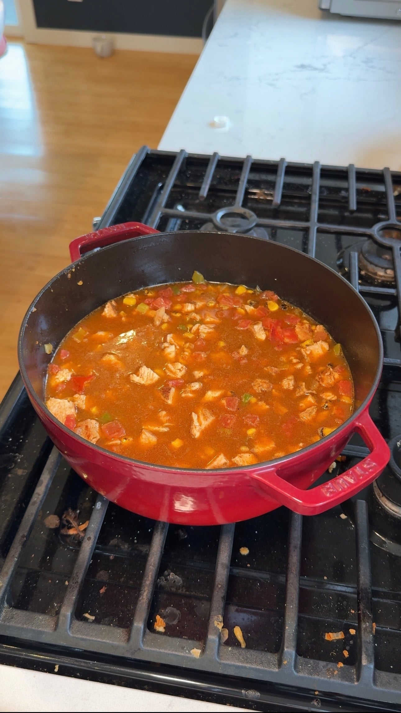 Chicken, corn, black beans, and Rotel simmering in broth in a red Dutch oven.