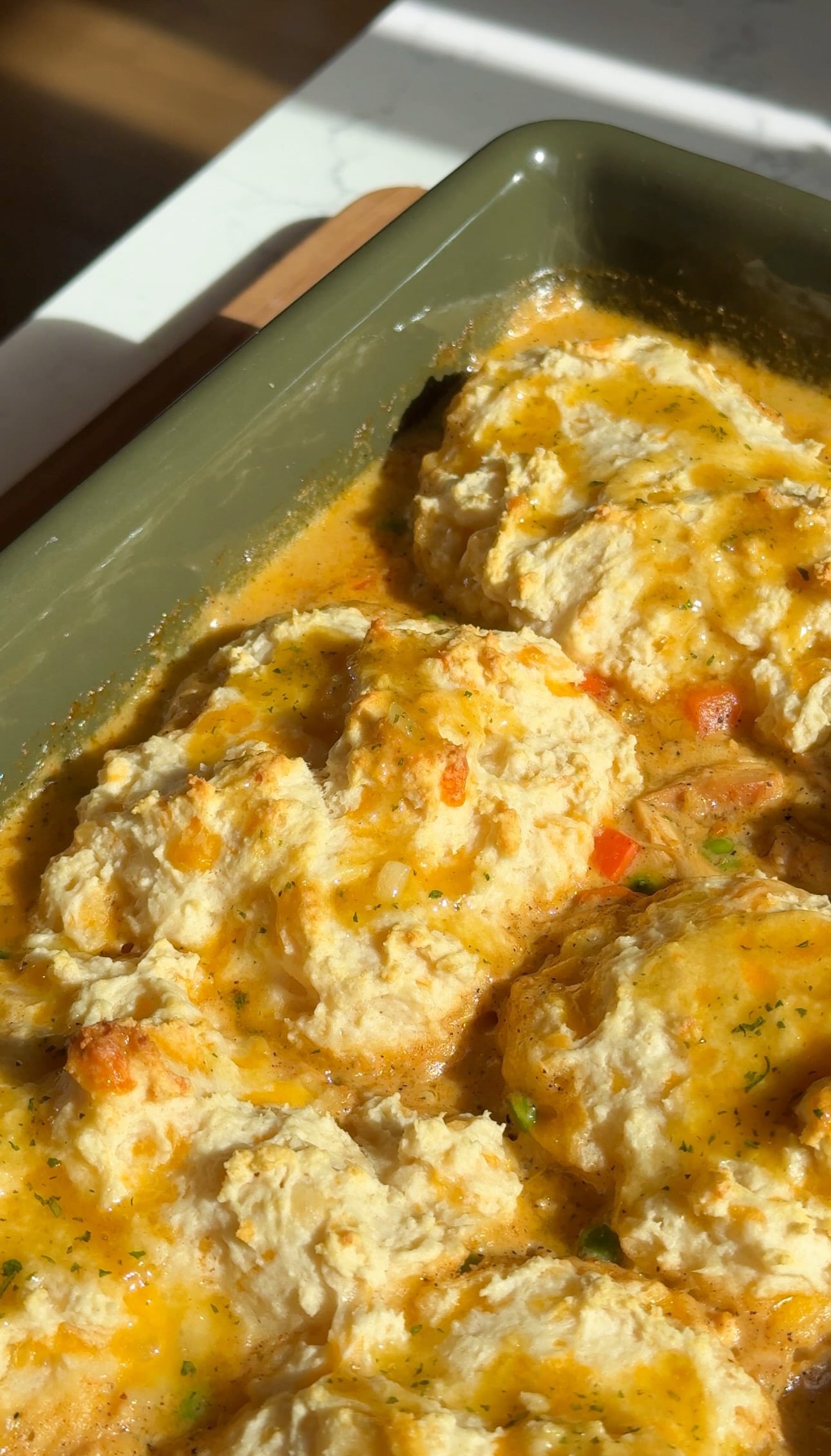 Cheddar bay biscuit chicken pot pie with golden garlic butter biscuits in a green baking dish.