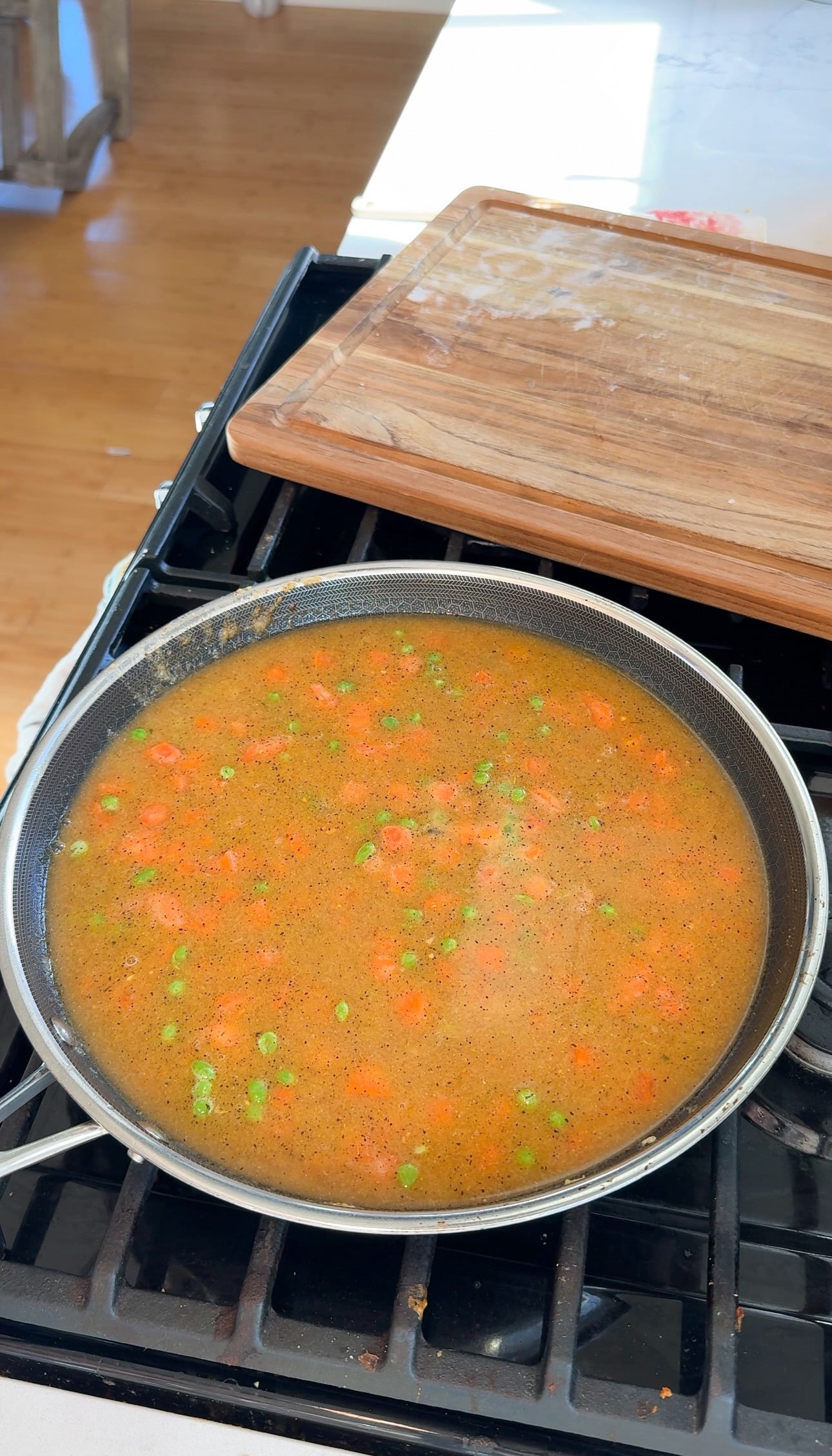 Chicken stock, peas, and carrots simmering in a large pan for chicken pot pie filling.