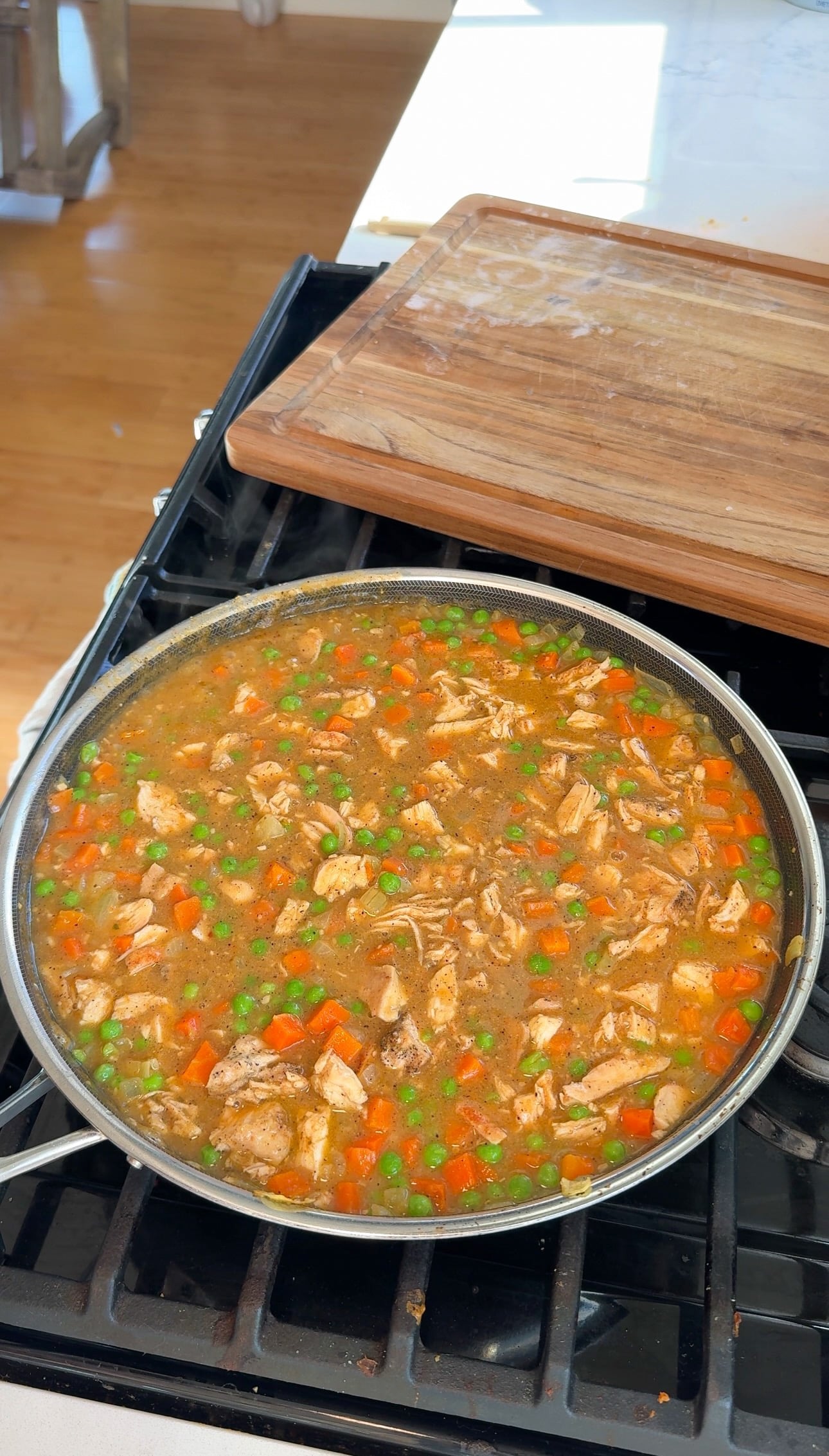 Diced chicken stirred into the creamy cowboy butter pot pie filling in a skillet.