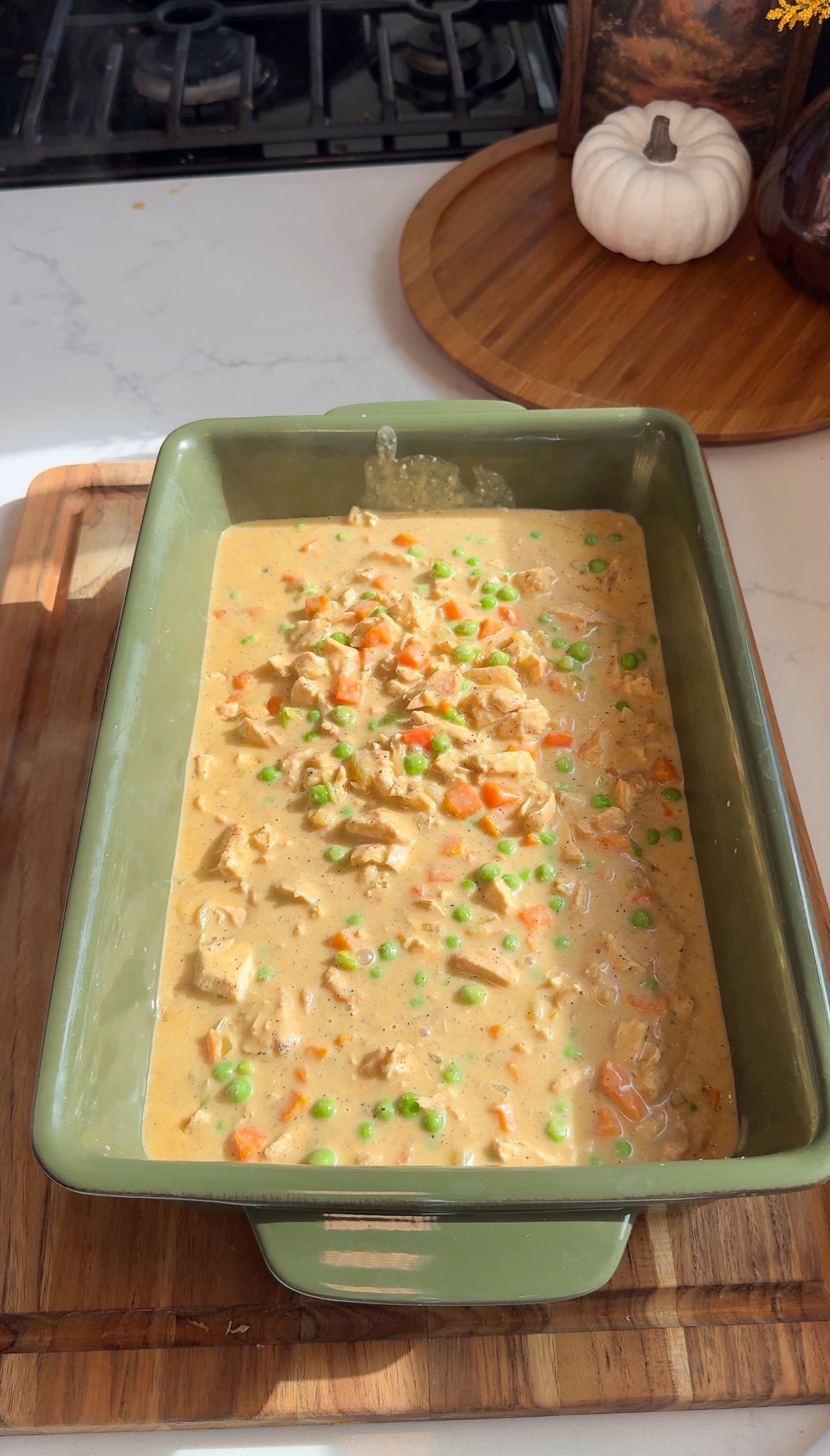 Creamy chicken, pea, and carrot pot pie filling spread in a green 9x13 casserole dish.