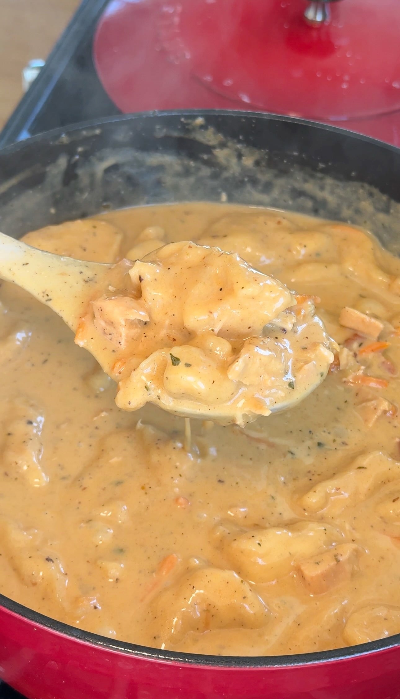 A wooden spoon lifting creamy chicken and dumplings with biscuit dumplings from the pot.