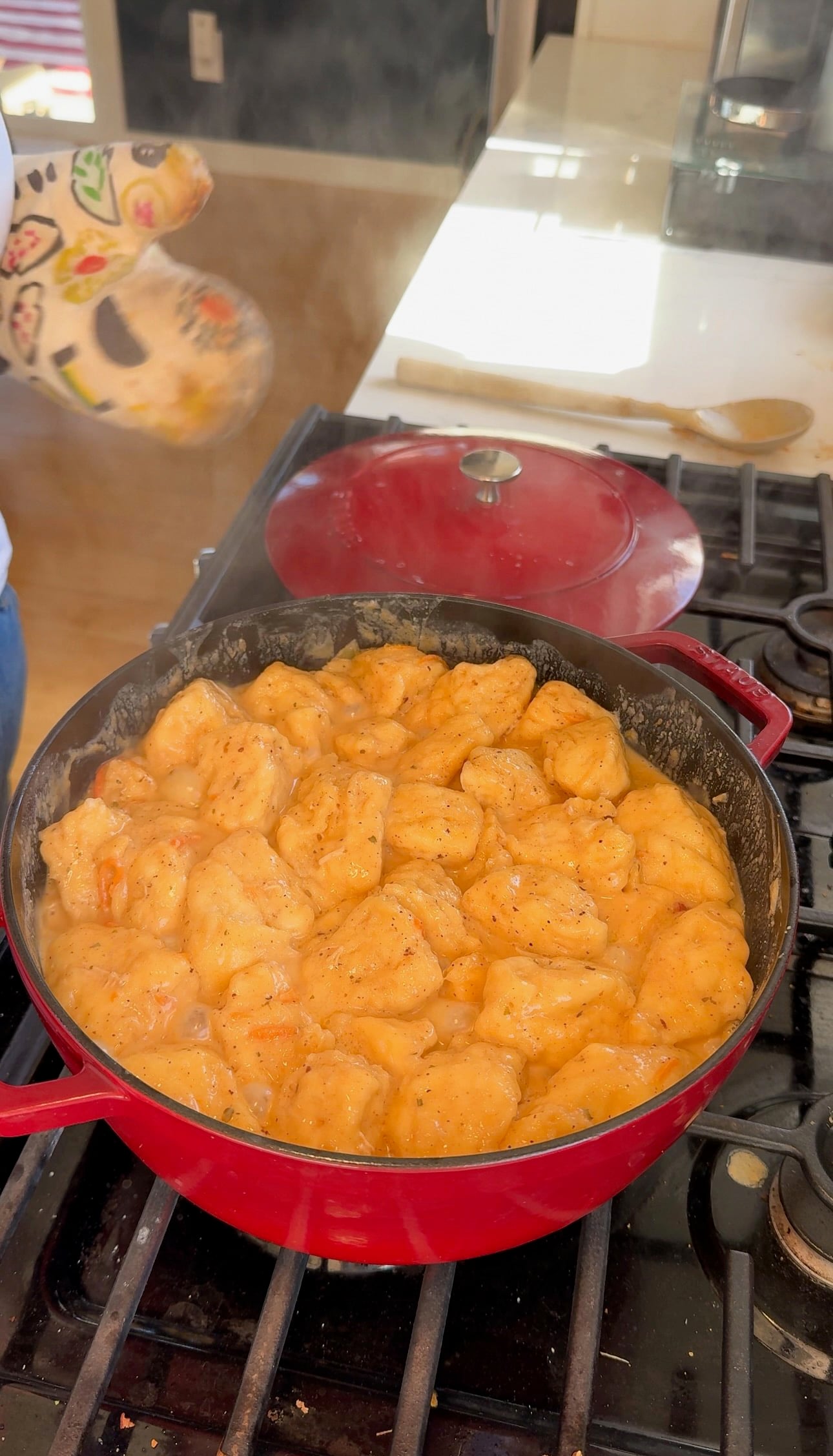 Fluffy biscuit dumplings cooked in creamy chicken soup in a red Dutch oven.