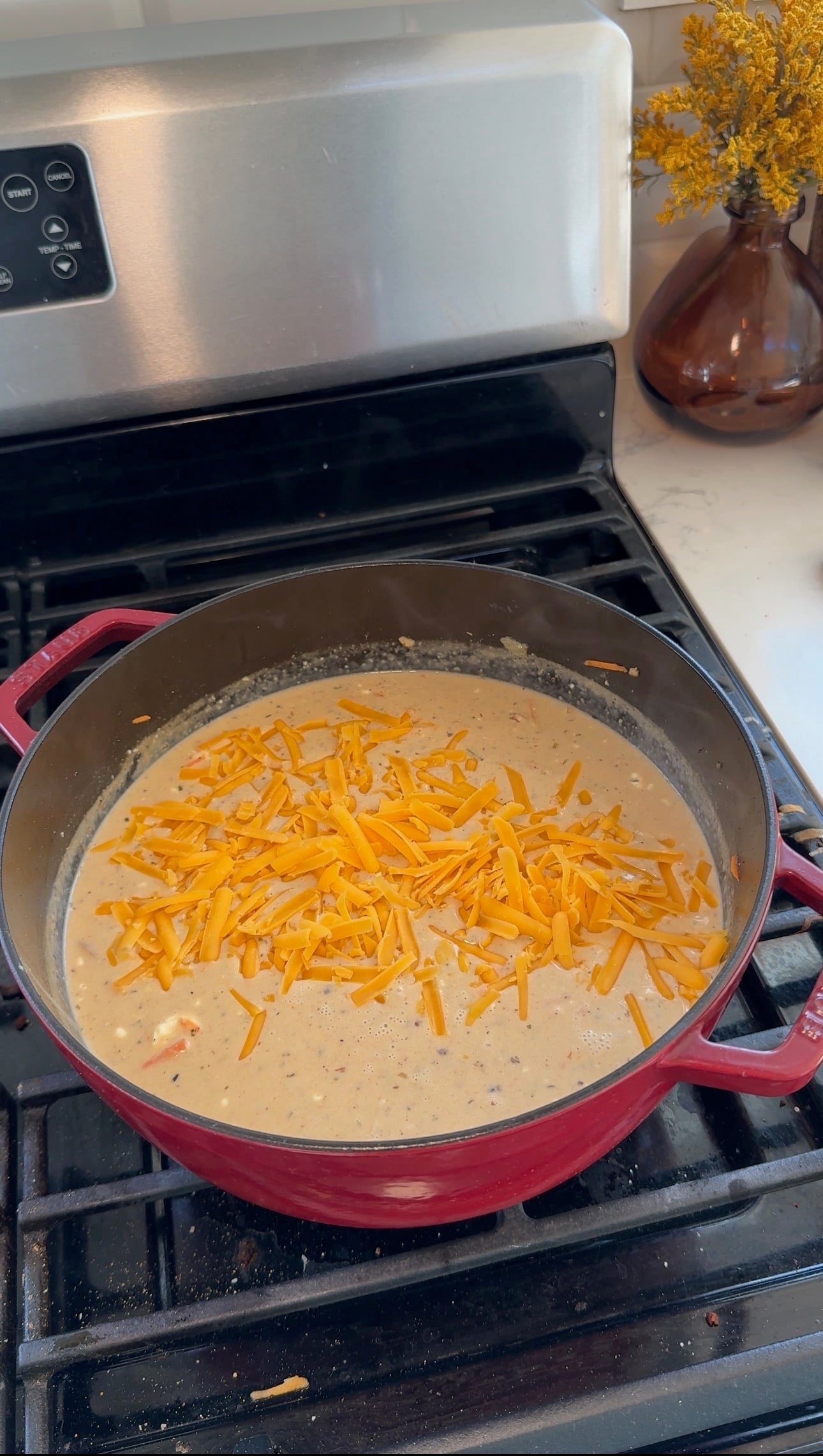 Shredded sharp cheddar cheese added to creamy crack chicken soup on the stove.