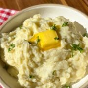 A bowl of creamy mashed potatoes topped with a pat of melting butter and fresh herbs.