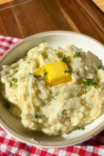 A bowl of creamy mashed potatoes topped with a pat of melting butter and fresh herbs.