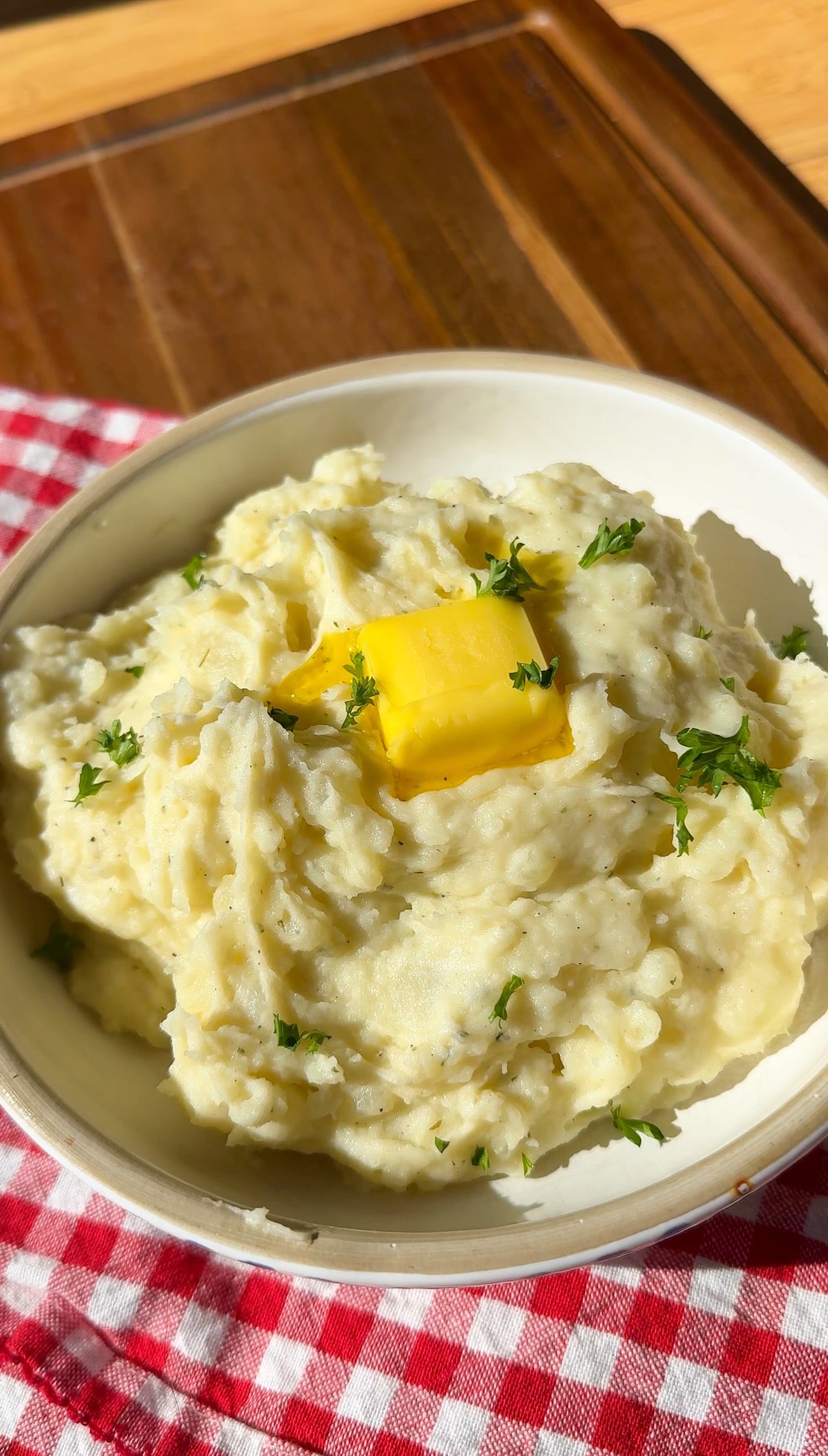 A bowl of creamy mashed potatoes topped with a pat of melting butter and fresh herbs.