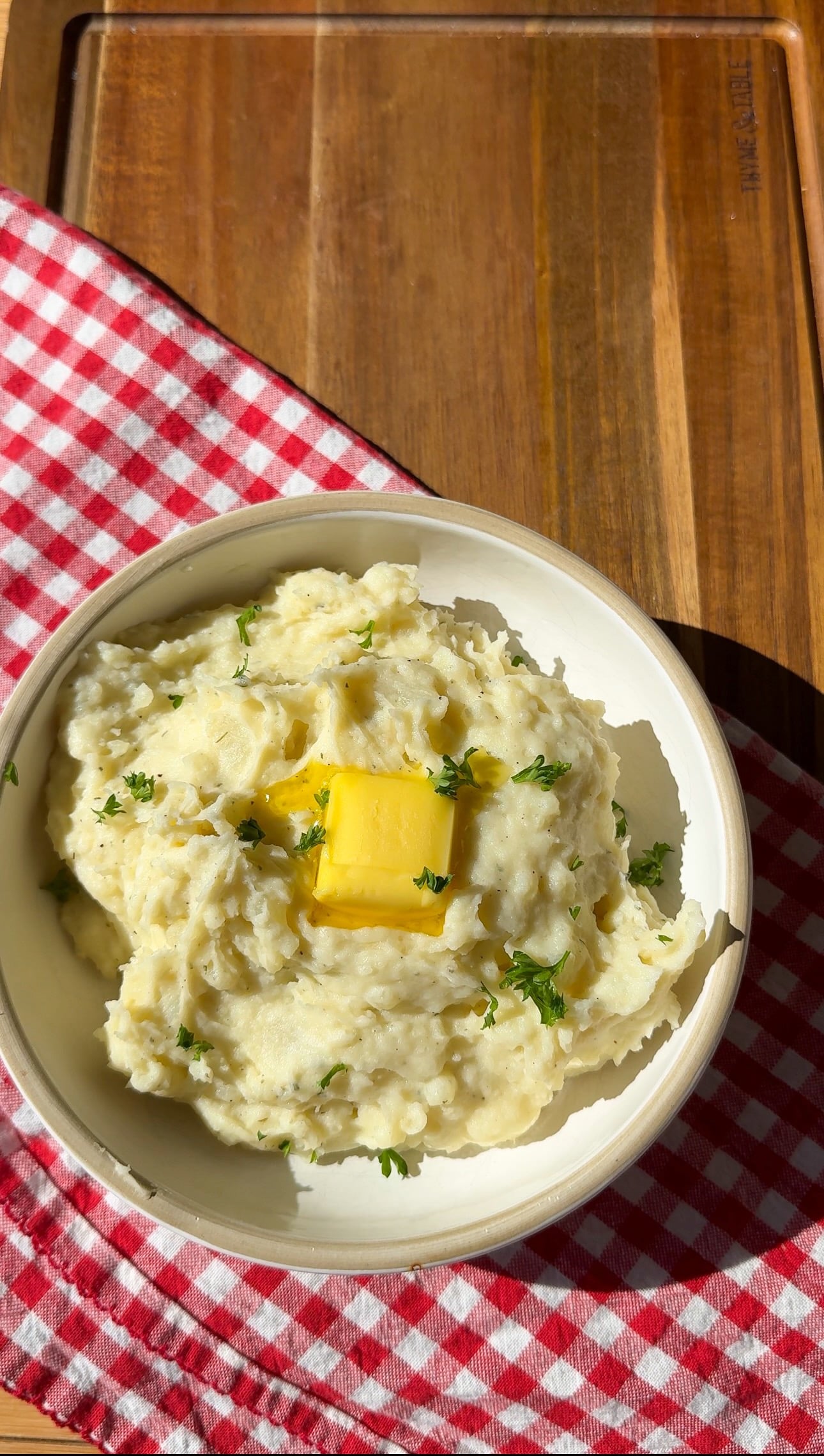 Easy mashed potatoes with melting butter and herbs in a bowl on a red plaid napkin.