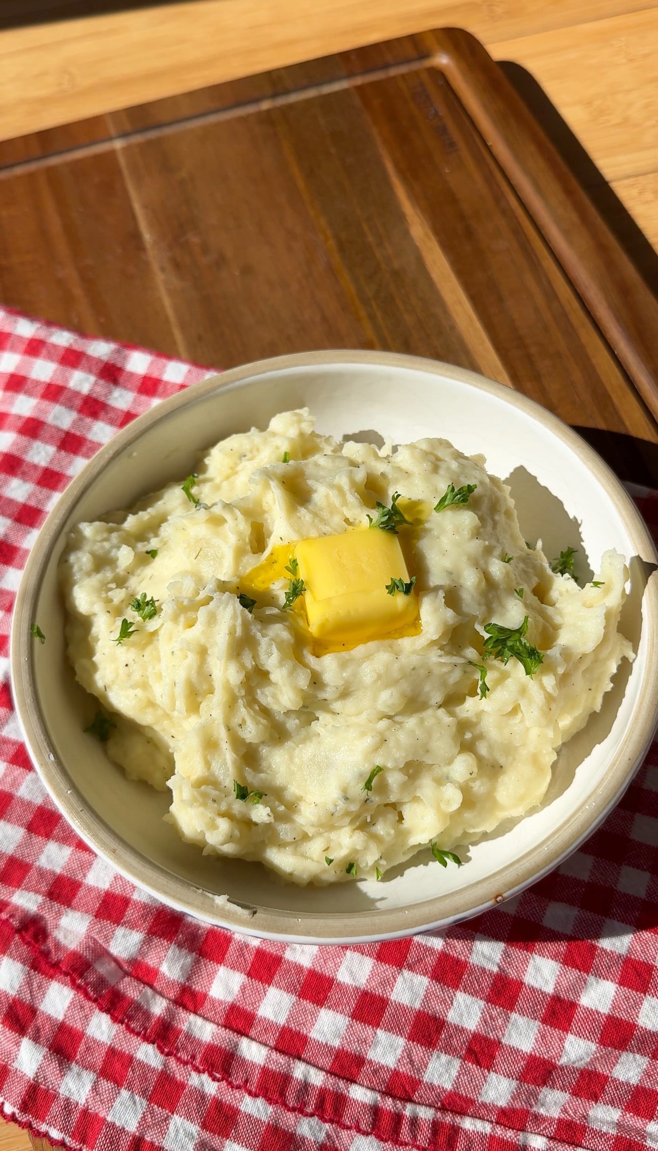 A bowl of sour cream mashed potatoes with butter and chopped herbs.