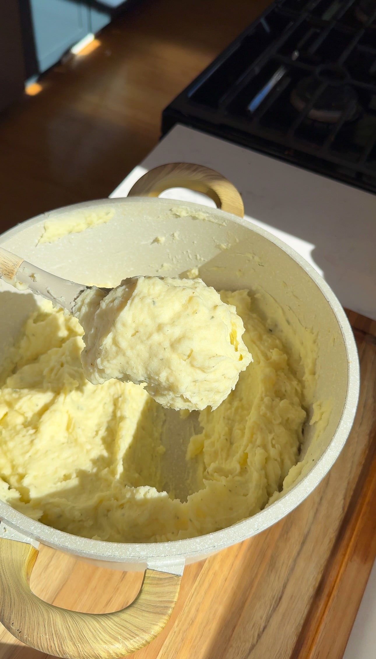 A wooden spoon lifting a scoop of smooth mashed potatoes from the pot.