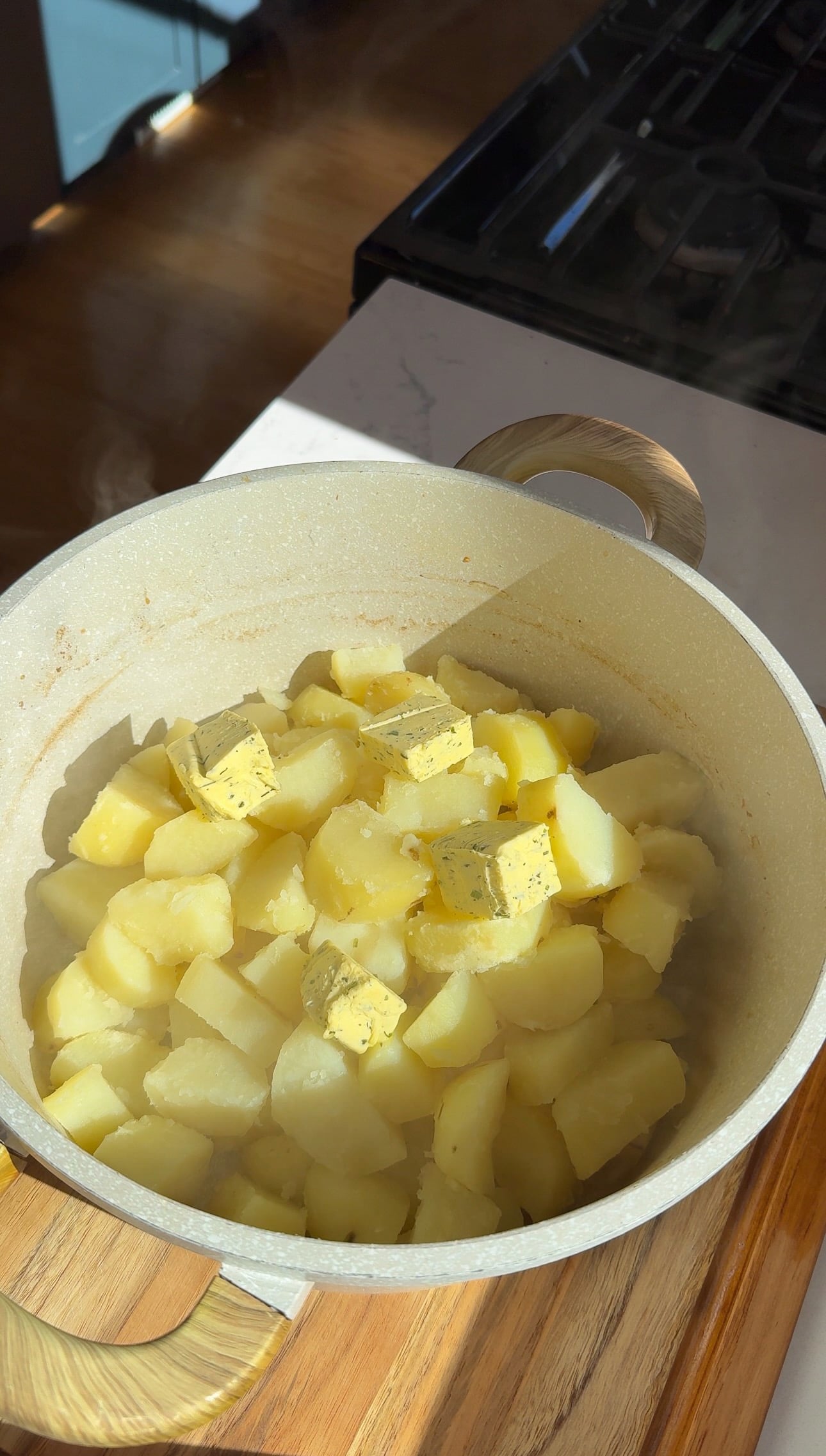 Drained boiled potatoes in a pot topped with cubes of garlic and herb butter.