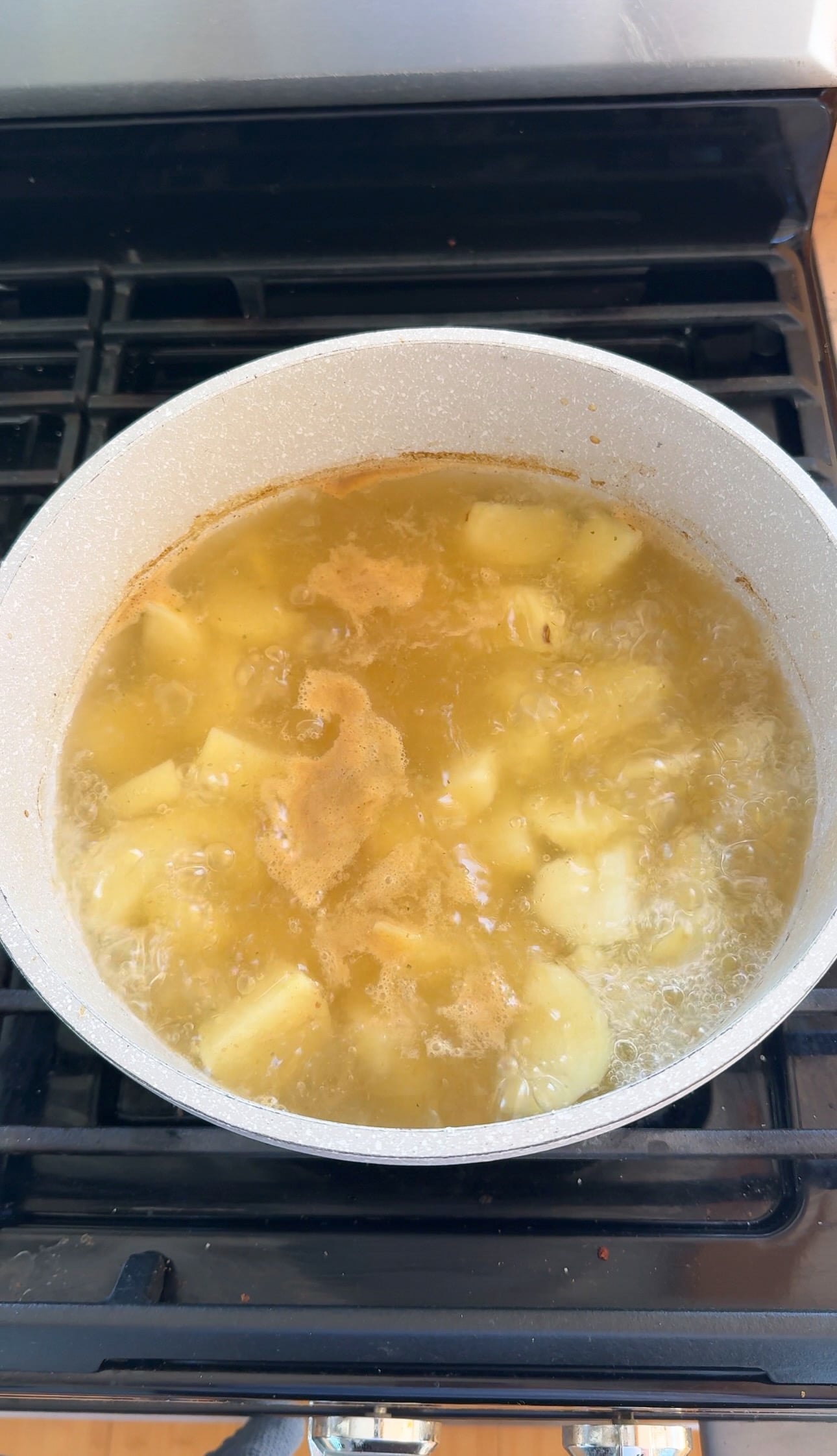 Peeled russet potatoes boiling in chicken bouillon water in a large pot on the stovetop.