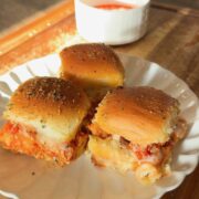 Three meatball sliders on a white scalloped plate with a small bowl of dipping sauce.