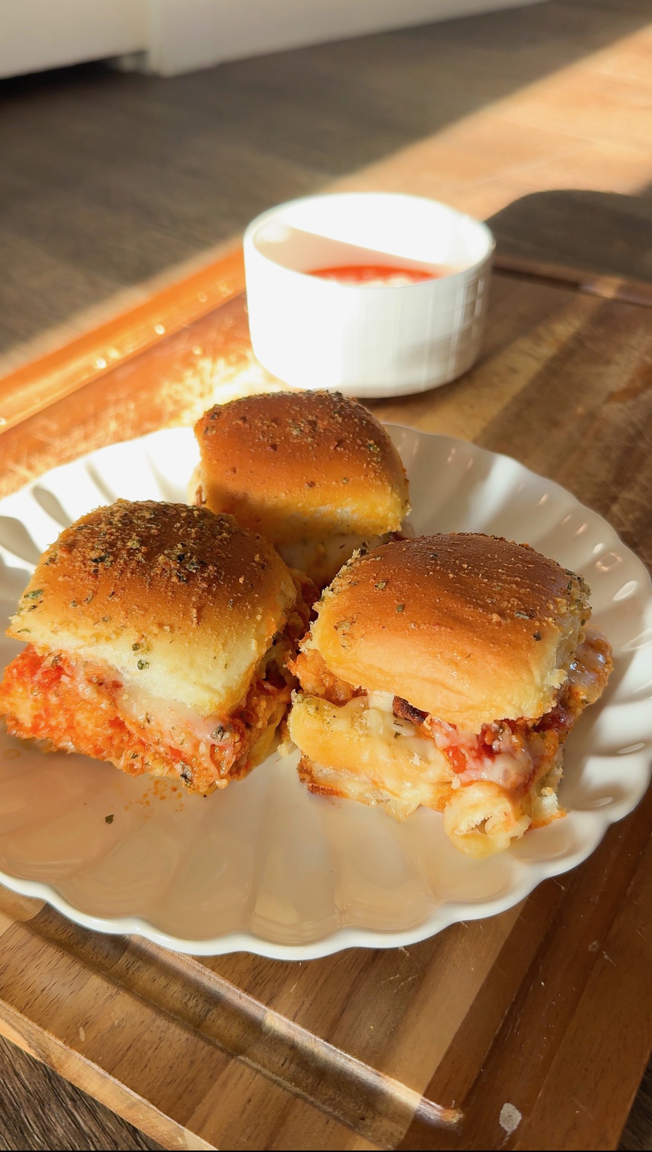 Three meatball sliders on a white scalloped plate with a small bowl of dipping sauce.