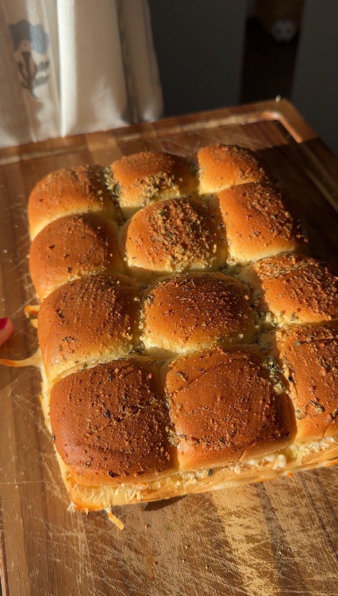 A tray of twelve baked garlic herb slider rolls on a wooden cutting board.