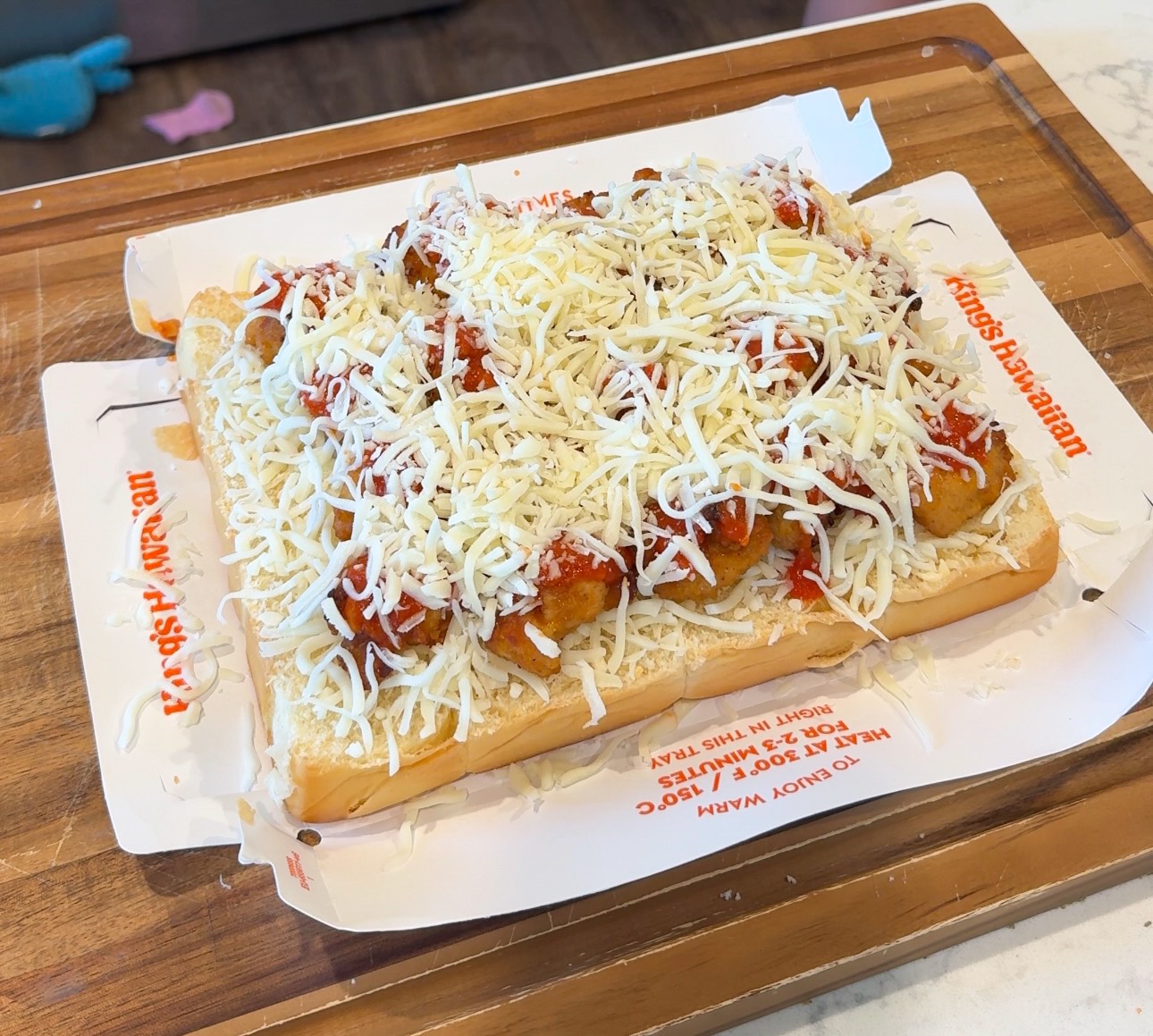 A Kings Hawaiian sub roll topped with chicken nuggets, tomato sauce, and shredded mozzarella cheese.