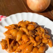 A plate of shell pasta in a creamy tomato and meat sauce, with a whole onion nearby.