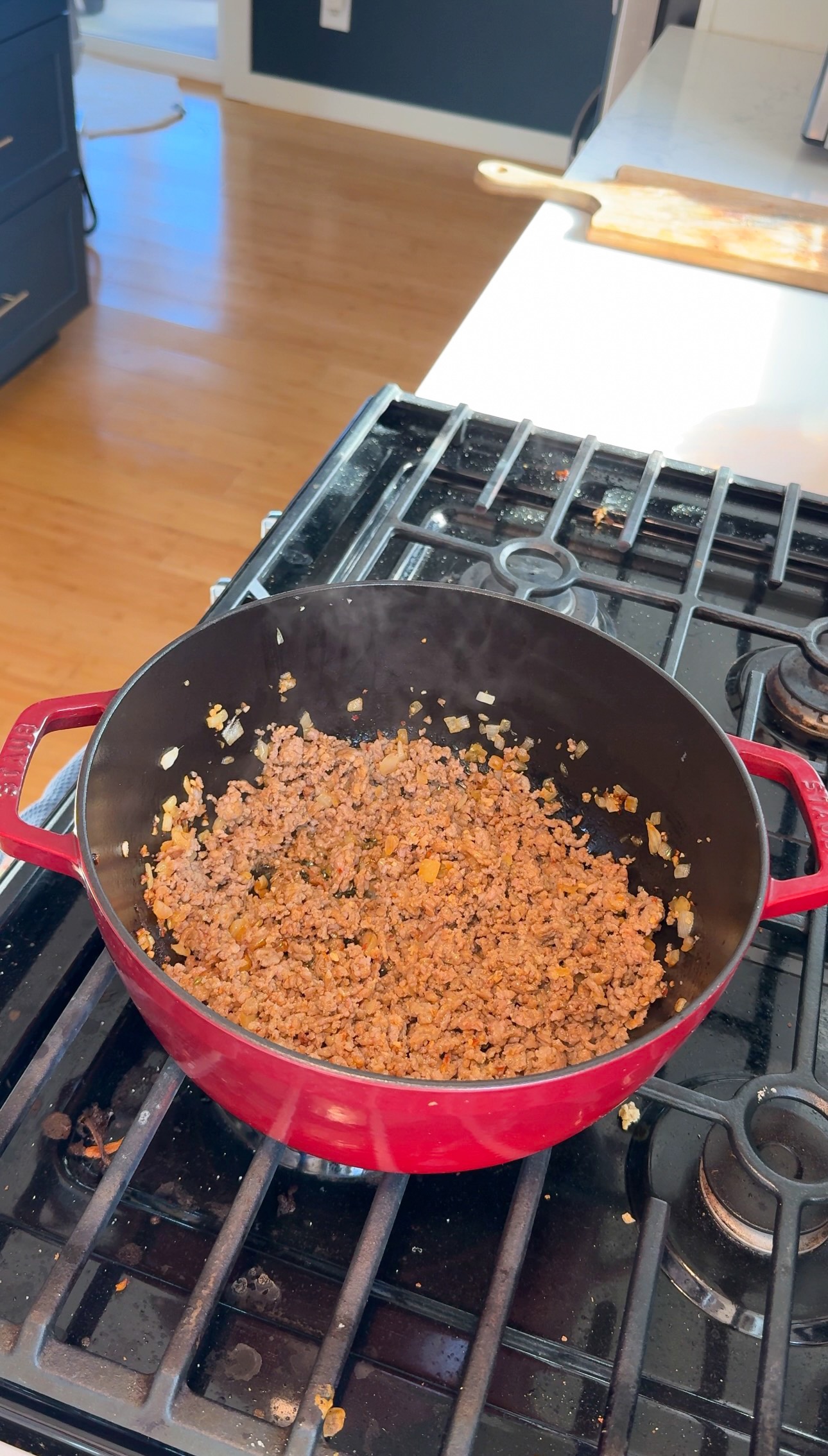 Ground meat browning with onions in a red enameled cast iron pot on a stovetop.