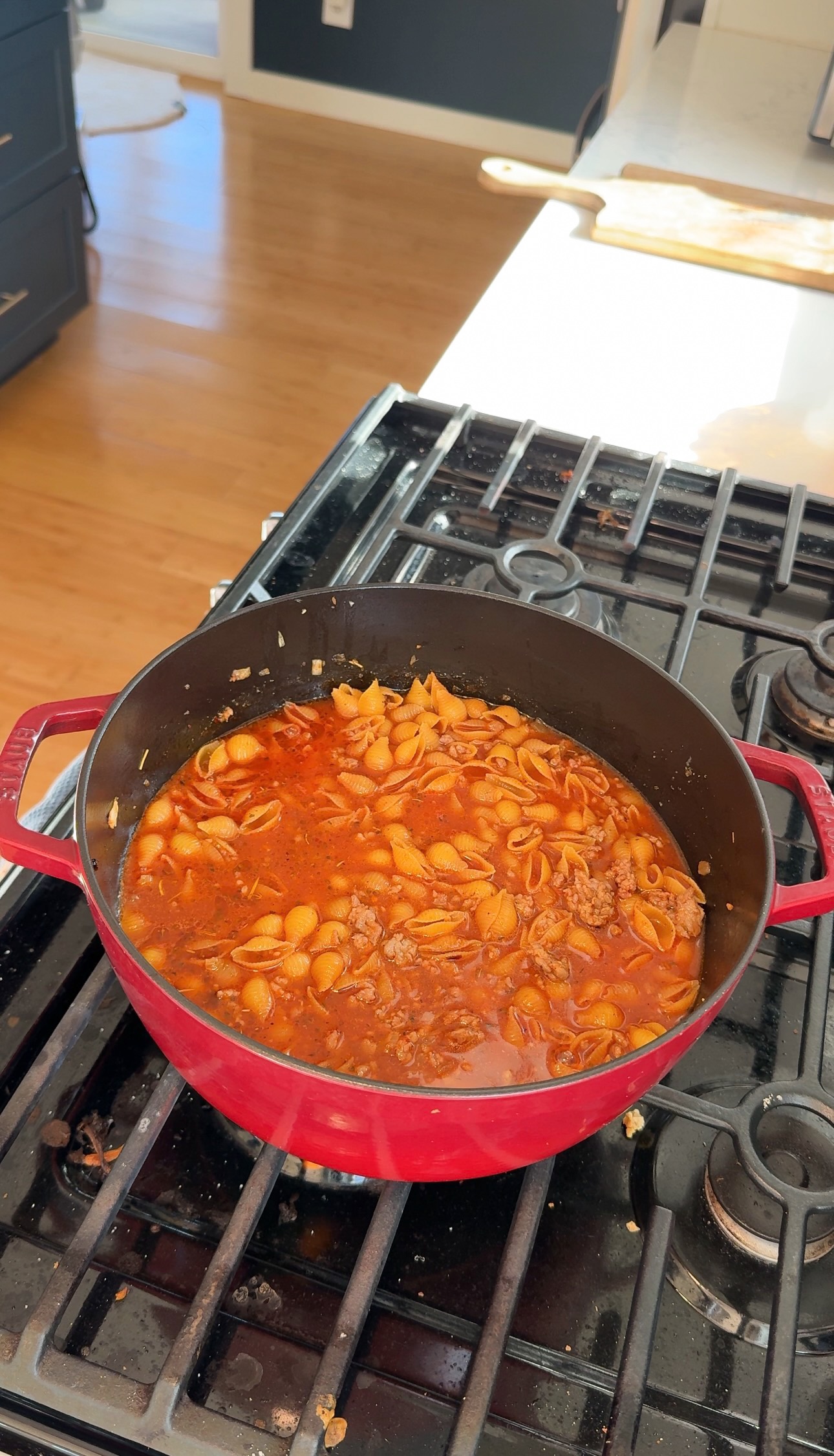A red enameled cast iron pot on a stovetop filled with shell pasta and ground meat in a tomato-based sauce.