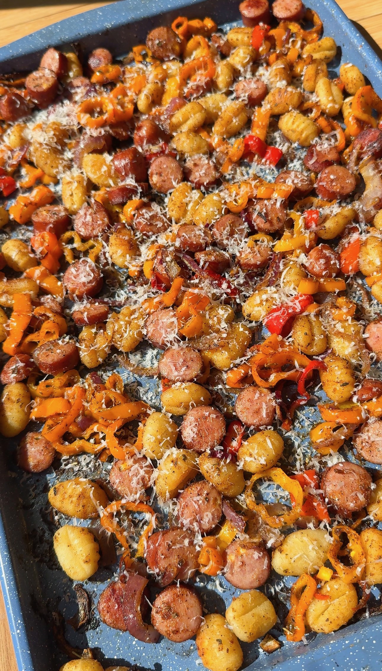 Sheet pan meal of roasted gnocchi, sliced sausage, and bell peppers topped with grated cheese.