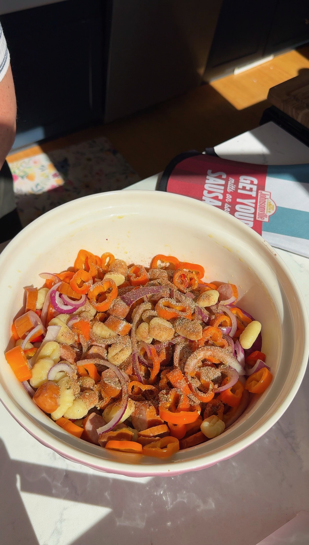 A bowl containing sliced orange peppers, red onion, and sausage pieces, topped with seasoning.