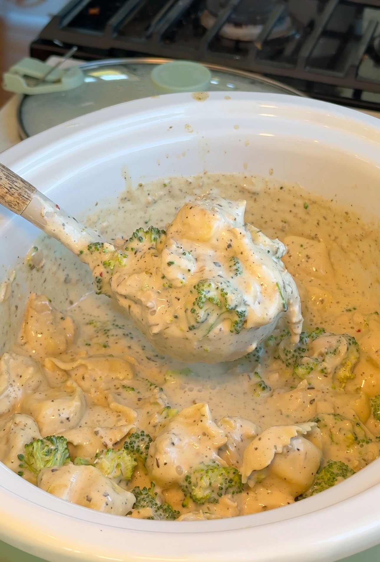 A spoonful of creamy broccoli tortellini soup lifted from a slow cooker.