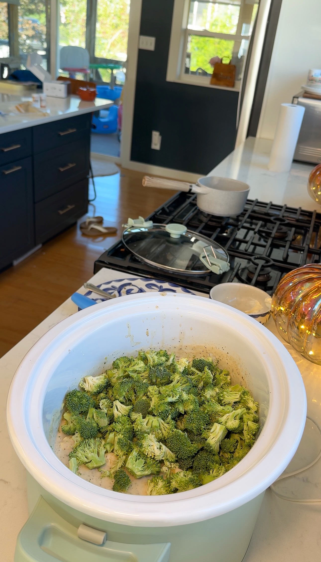 A slow cooker filled with raw broccoli florets sitting on a kitchen counter.
