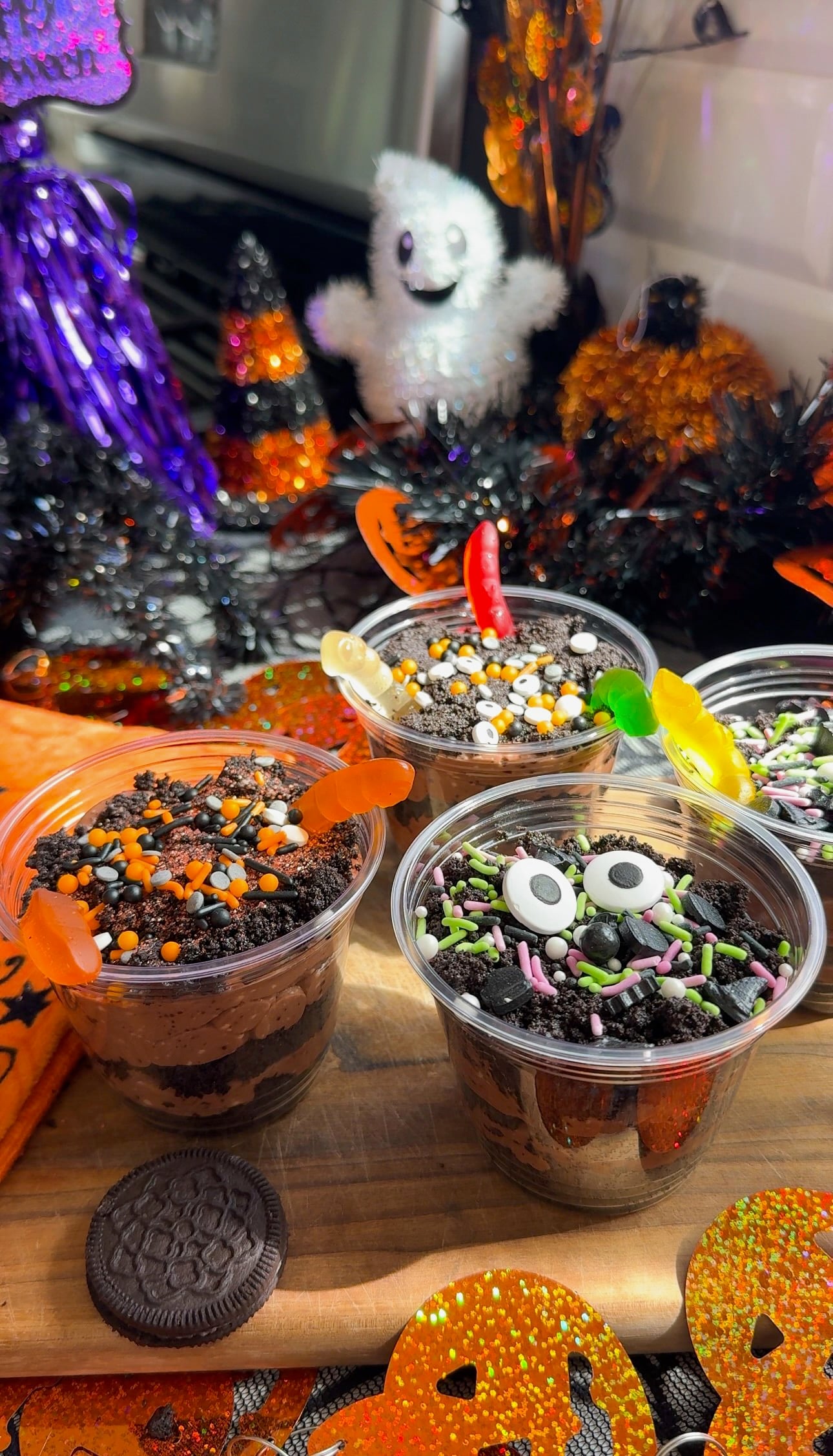 Clear cups of Oreo dirt cups layered with chocolate pudding and decorated with gummy worms, candy eyes, and Halloween sprinkles.